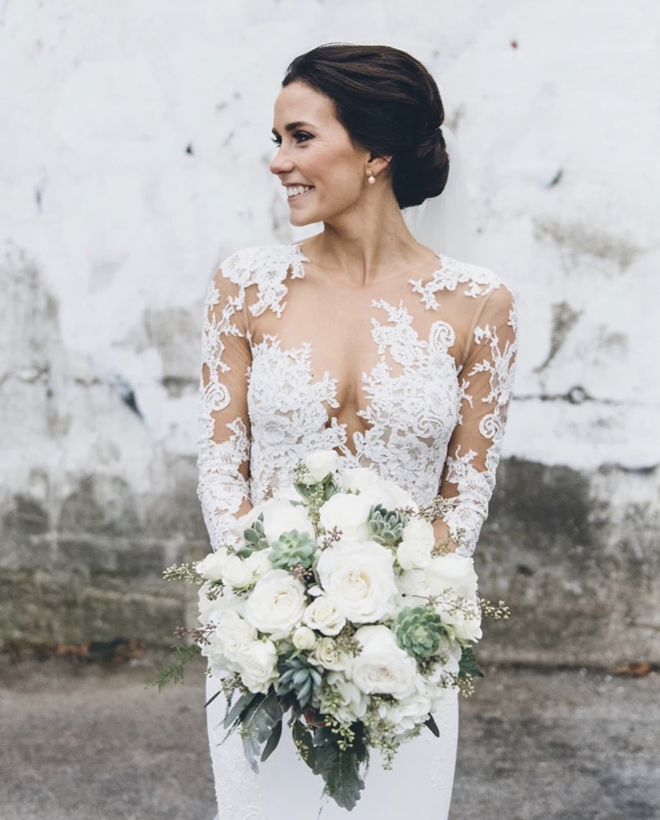 Bride in a lace gown with a soft updo, holding a white and succulent bouquet