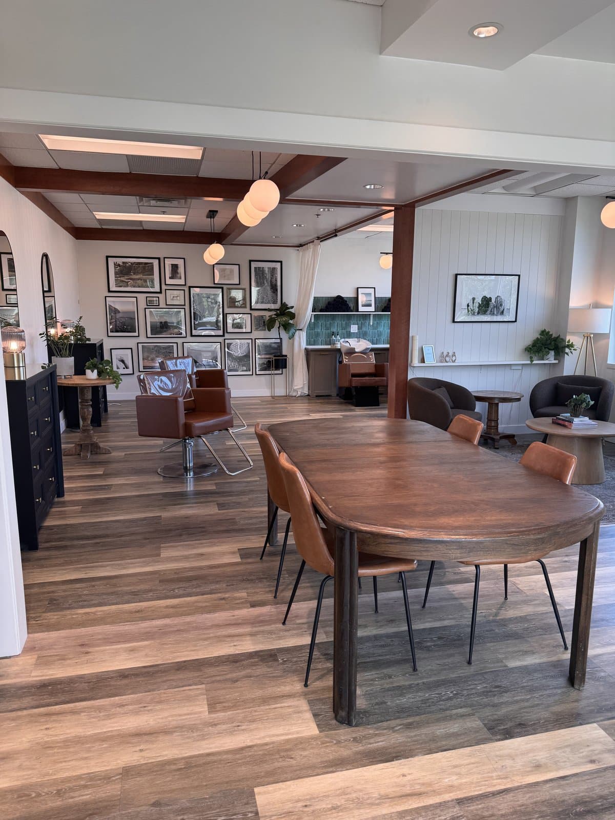 The main salon floor — styling chair, gallery wall, and a communal table